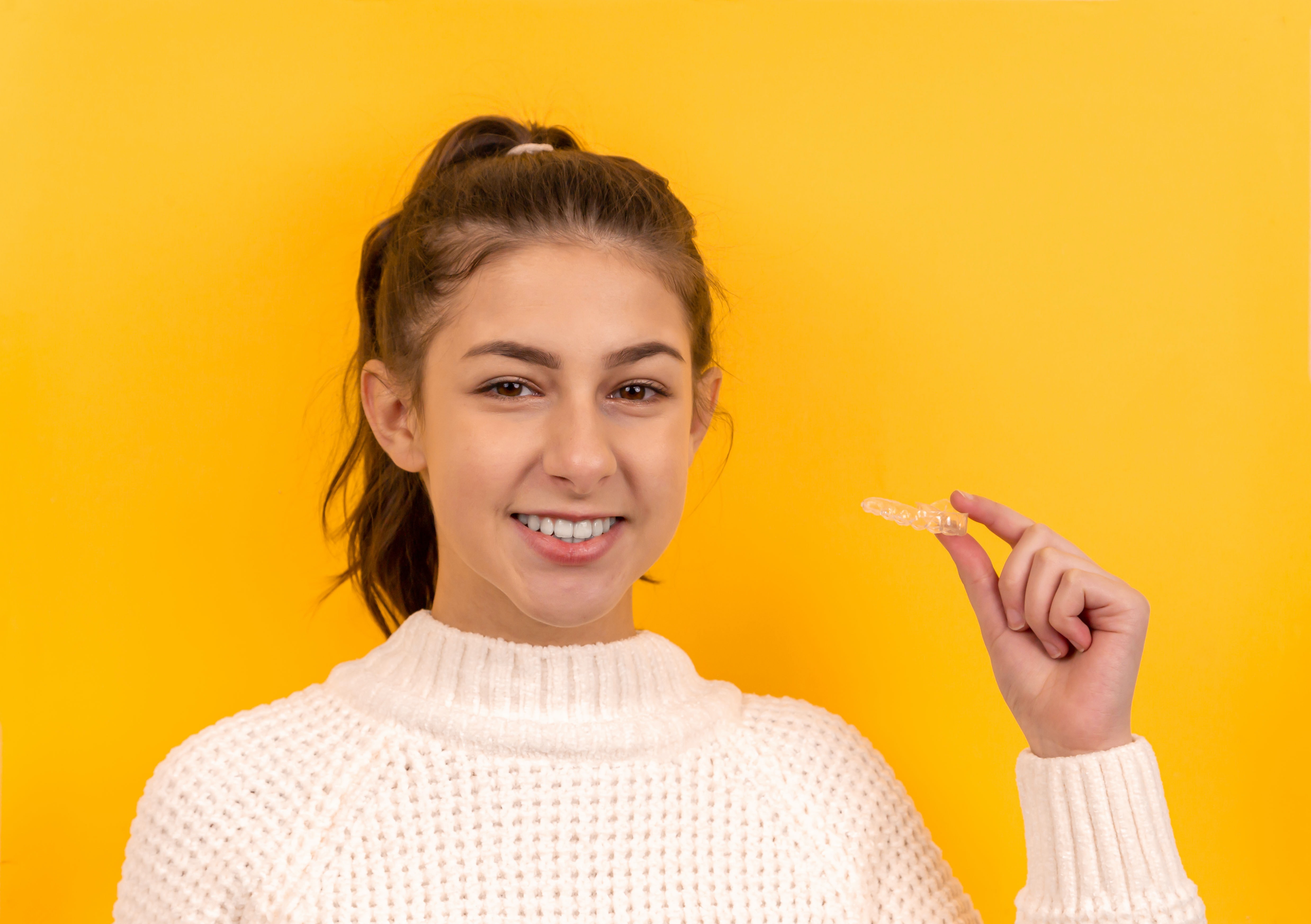 A woman holding up Invisalign against a yellow backround.