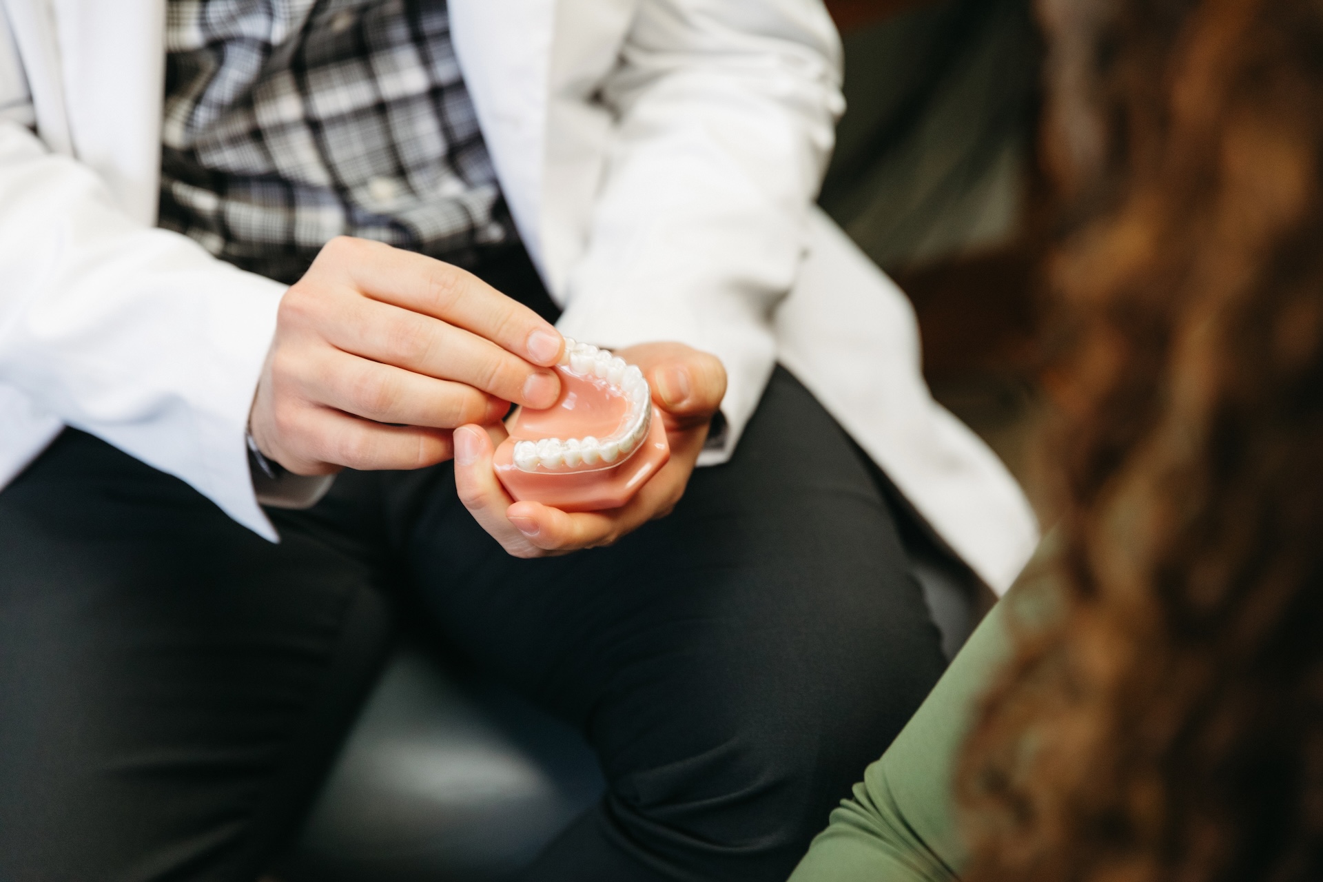 Dentist at Starbody Dental in white coat holding a dental model, explaining treatment to a patient with curly hair, seated nearby.