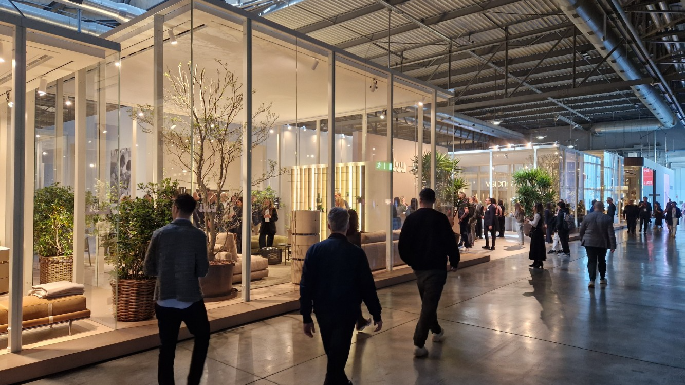A high-quality 3D render of a modern furniture exhibit at Salone del Mobile 2025, showcasing atmospheric lighting and detailed textures.