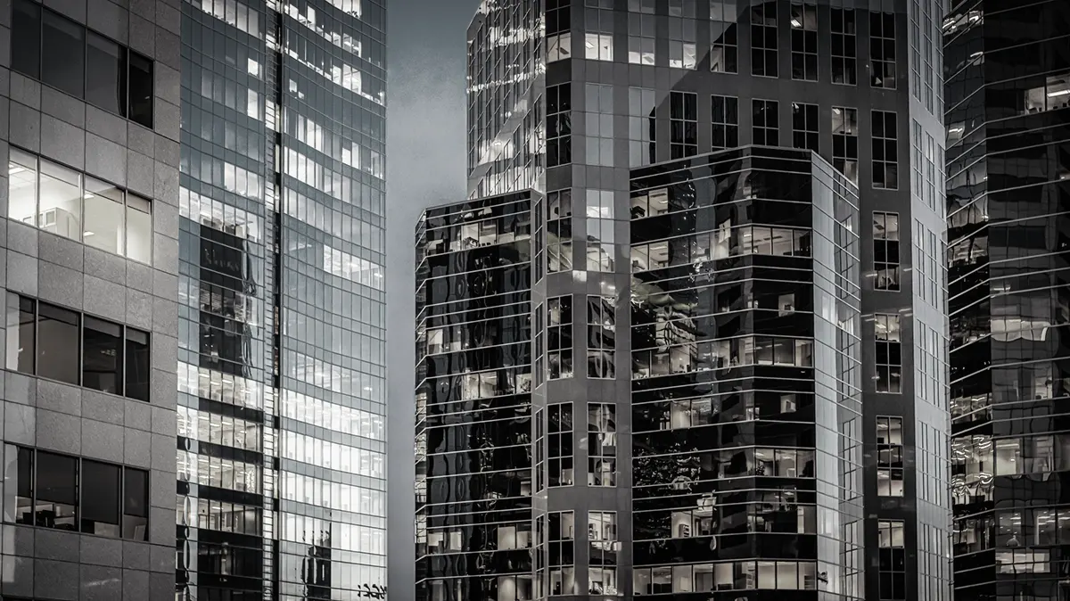 Looking upwards at tall modern skyscrapers with glass and steel facades converging towards the sky.