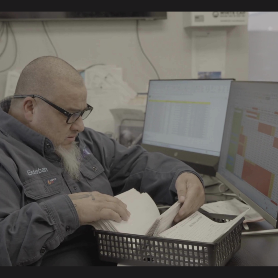 Oilfield worker sorting paper tickets and spreadsheets, highlighting inefficiencies compared to SCADA automation