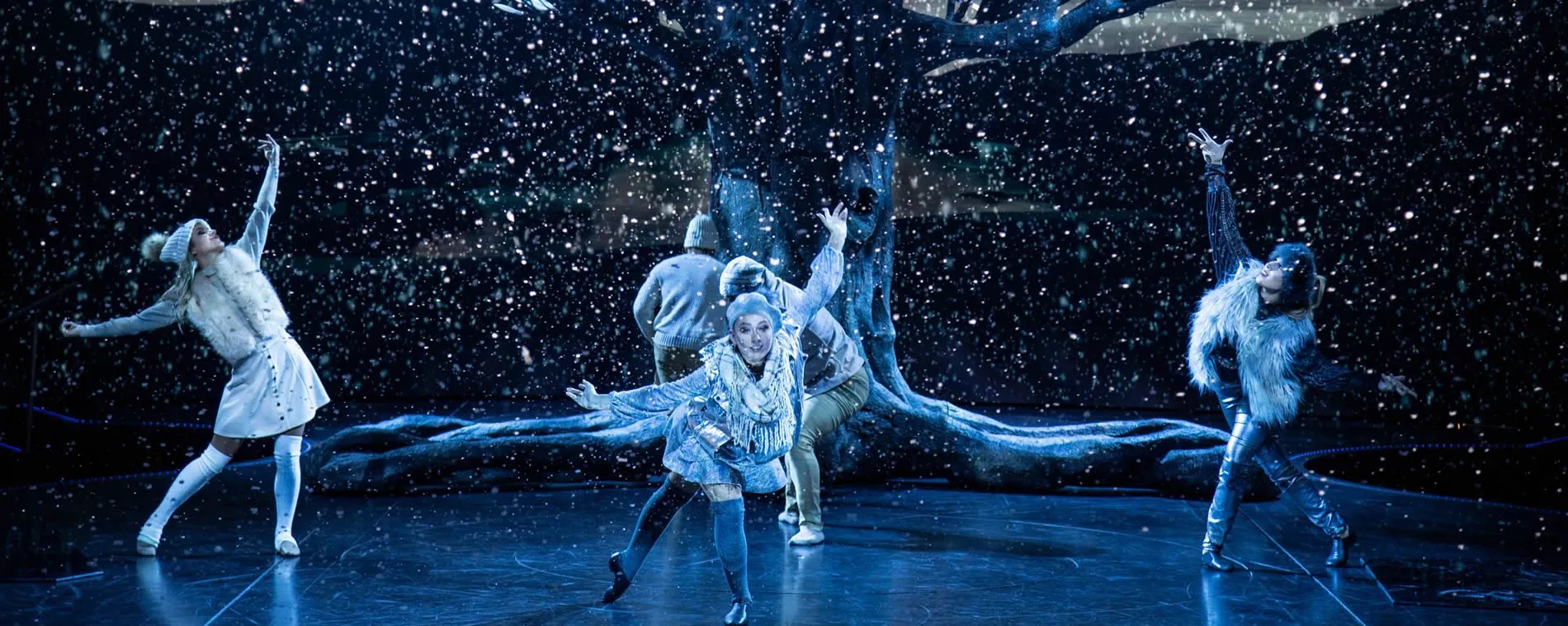 Dancers in winter costumes performing on stage with falling snowflakes