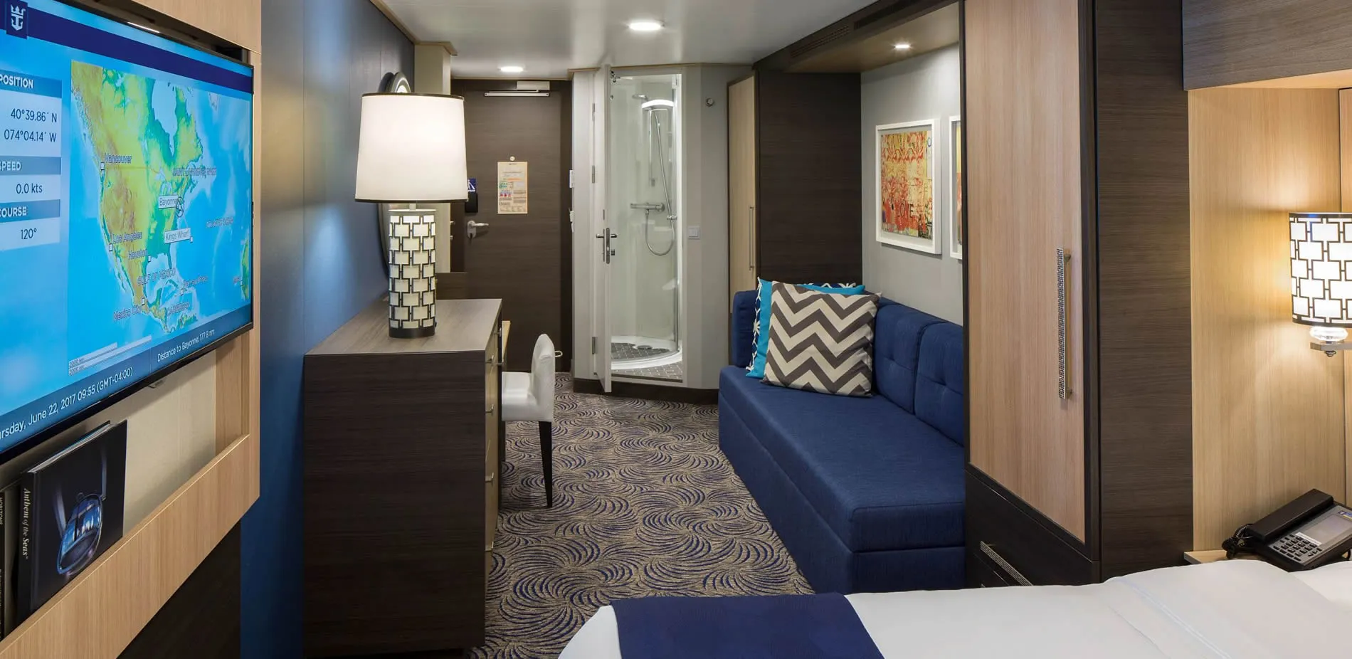 Modern cruise ship cabin with blue sofa, map screen, and white shower