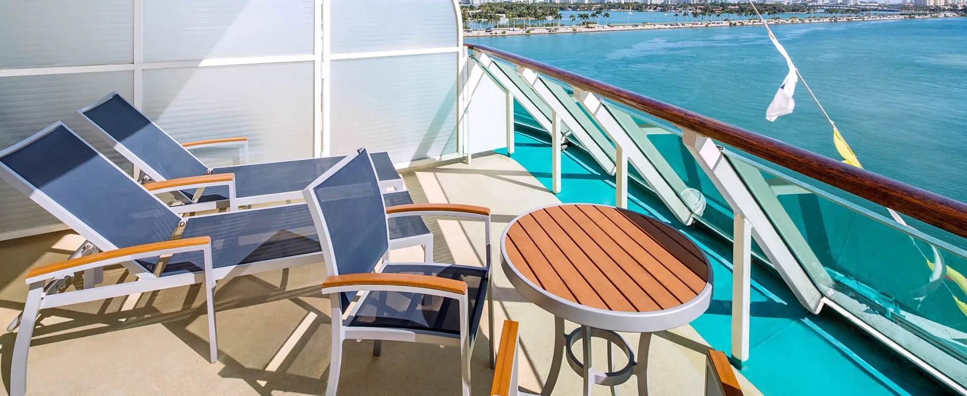 Cruise ship balcony with lounge chairs overlooking blue ocean and coastline