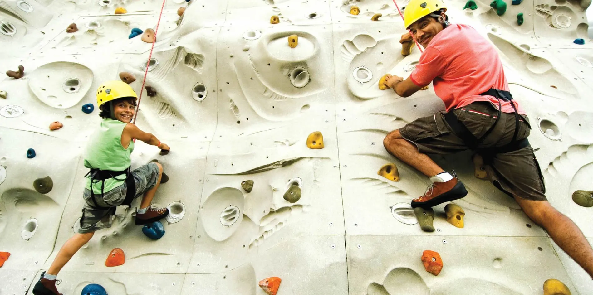 Parent and child climbing indoor rock wall with colorful safety gear