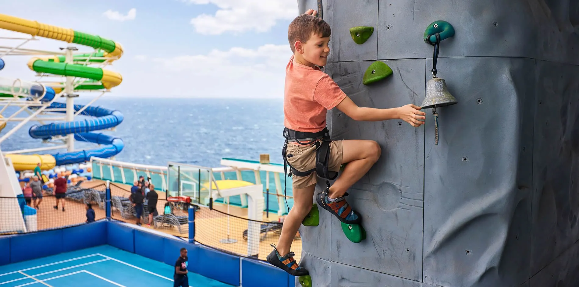 Child climbing rock wall on cruise ship with waterslides in background