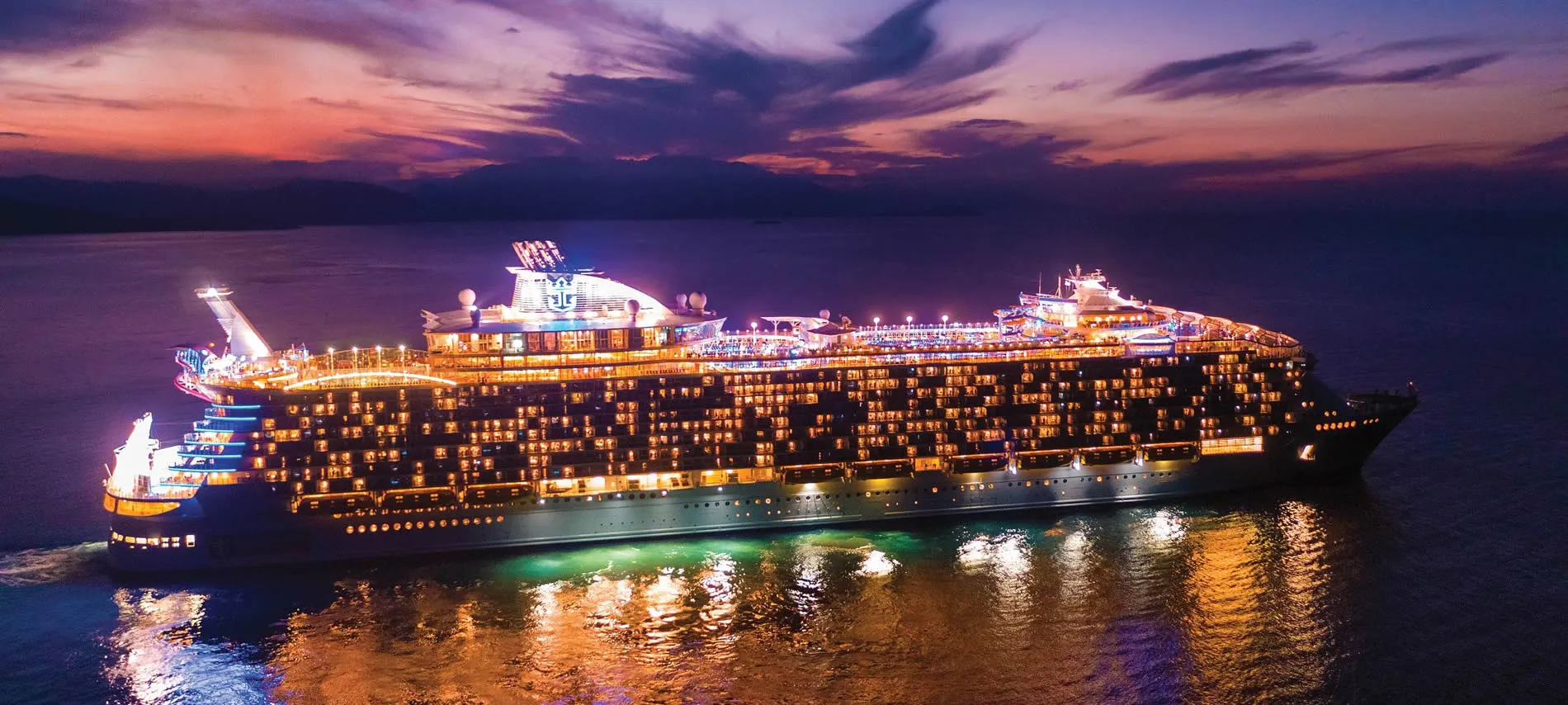 Large cruise ship illuminated at night with colorful sunset sky and ocean