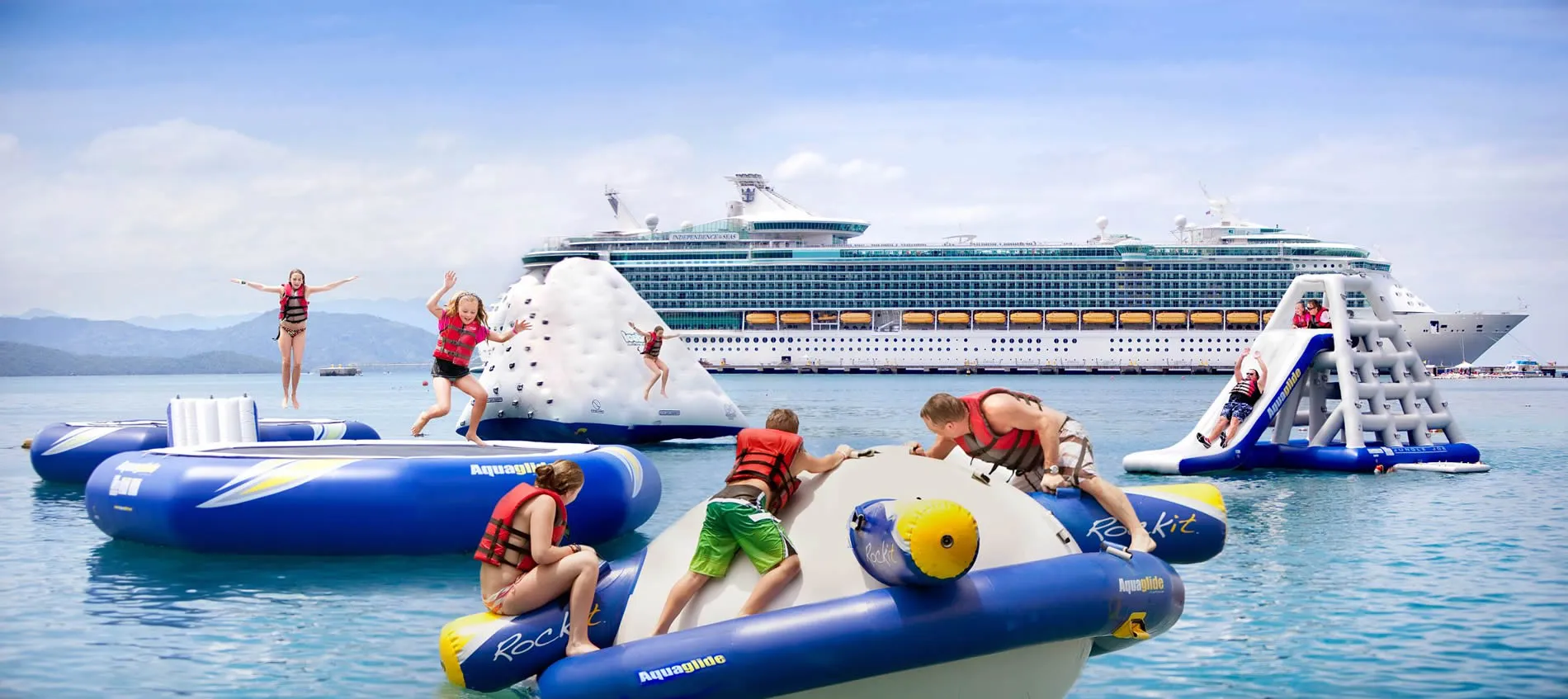 Children playing on inflatable water toys near large cruise ship