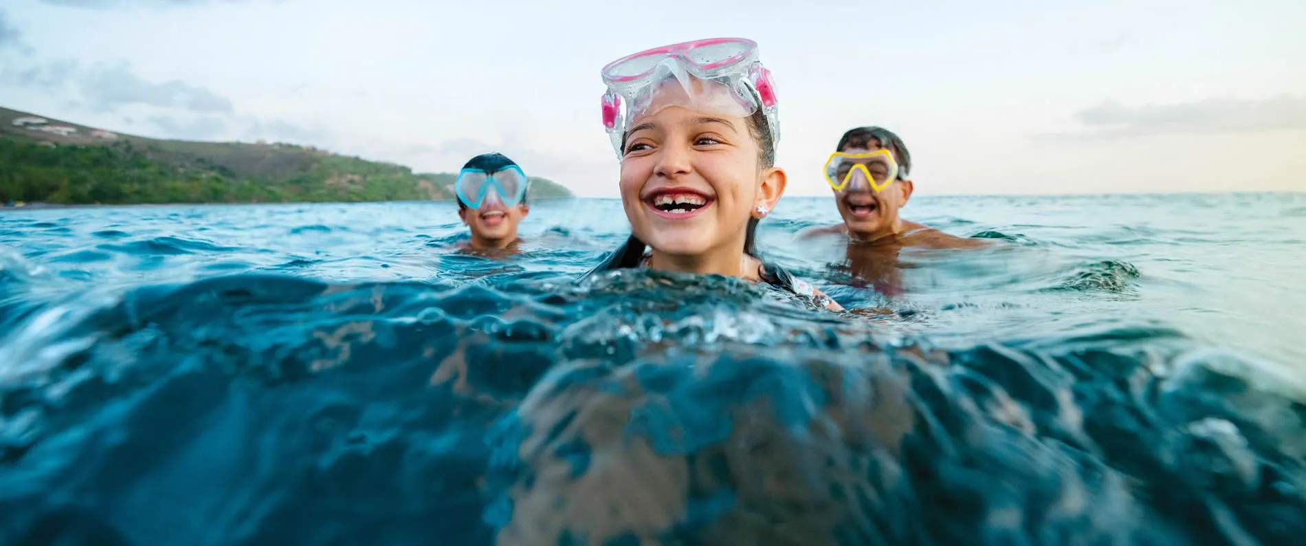 Children swimming and snorkeling, laughing in clear blue ocean water