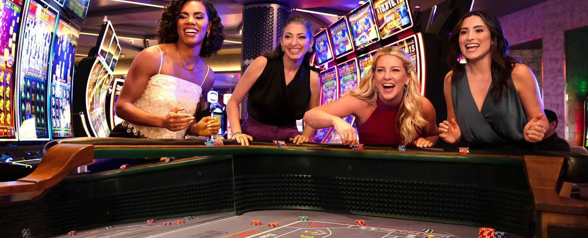 Four women enjoying themselves at a casino gambling table with slot machines