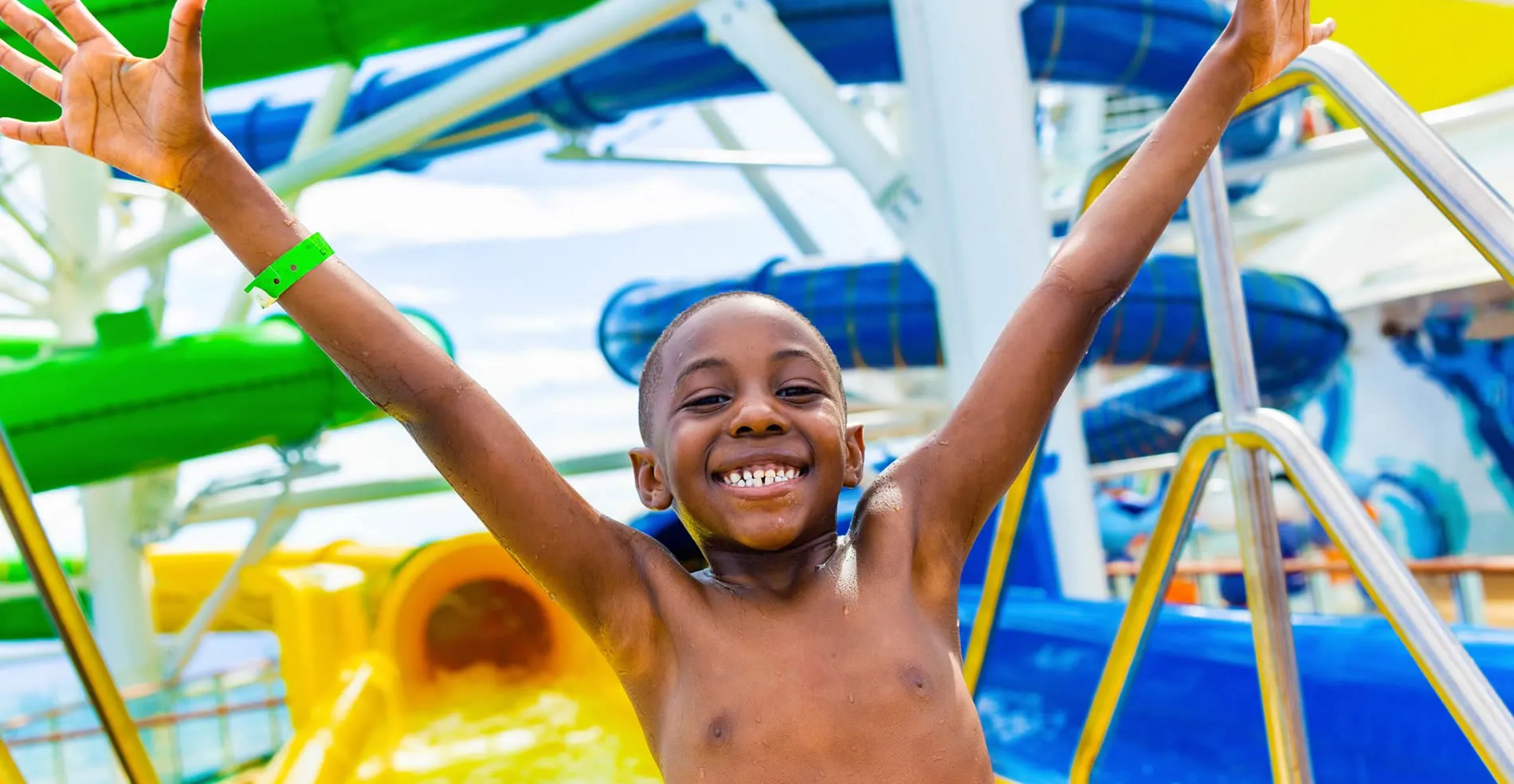 Excited child with raised arms at colorful water park water slides