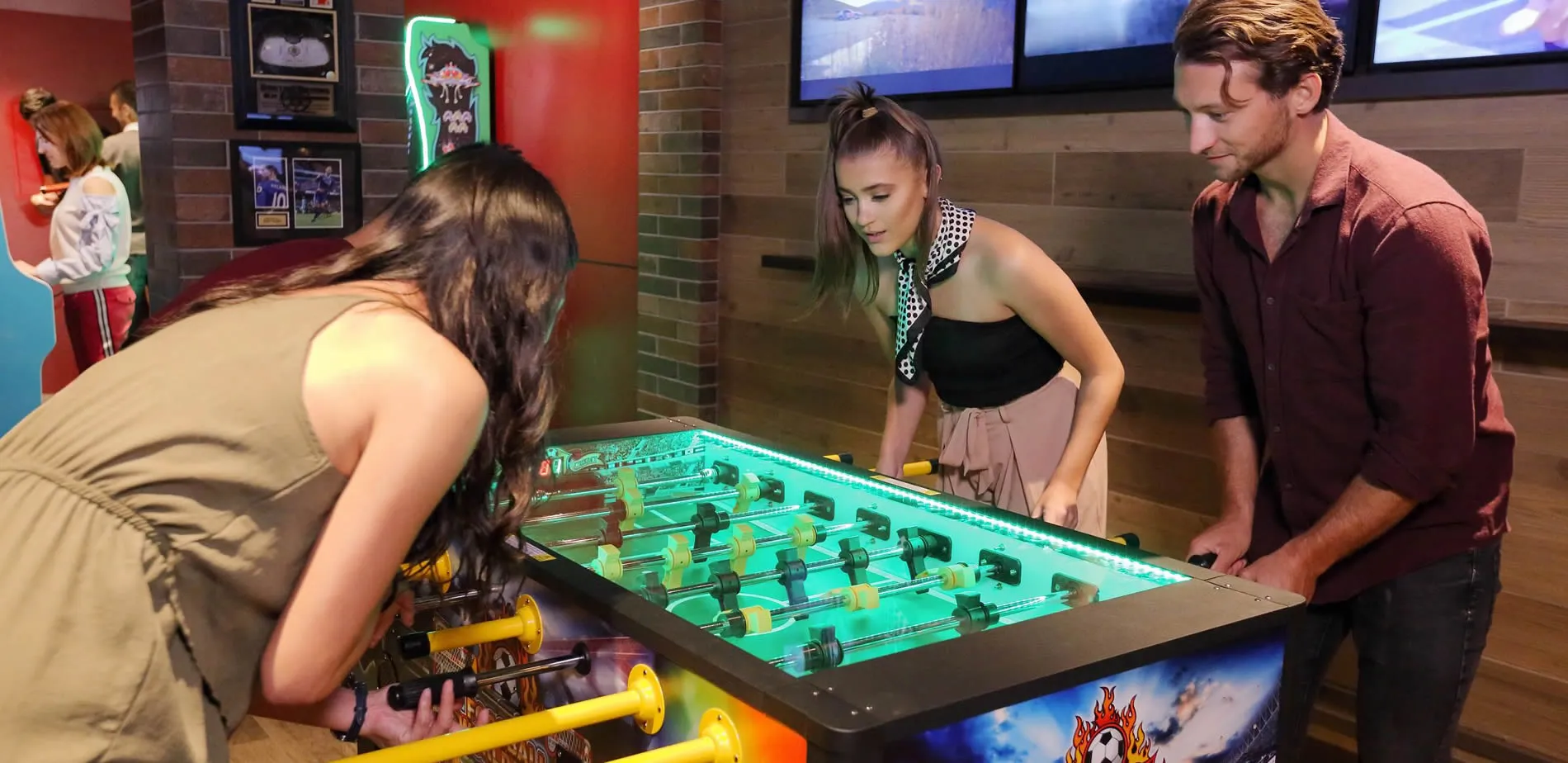 Friends playing foosball on a glowing green table in a recreational room