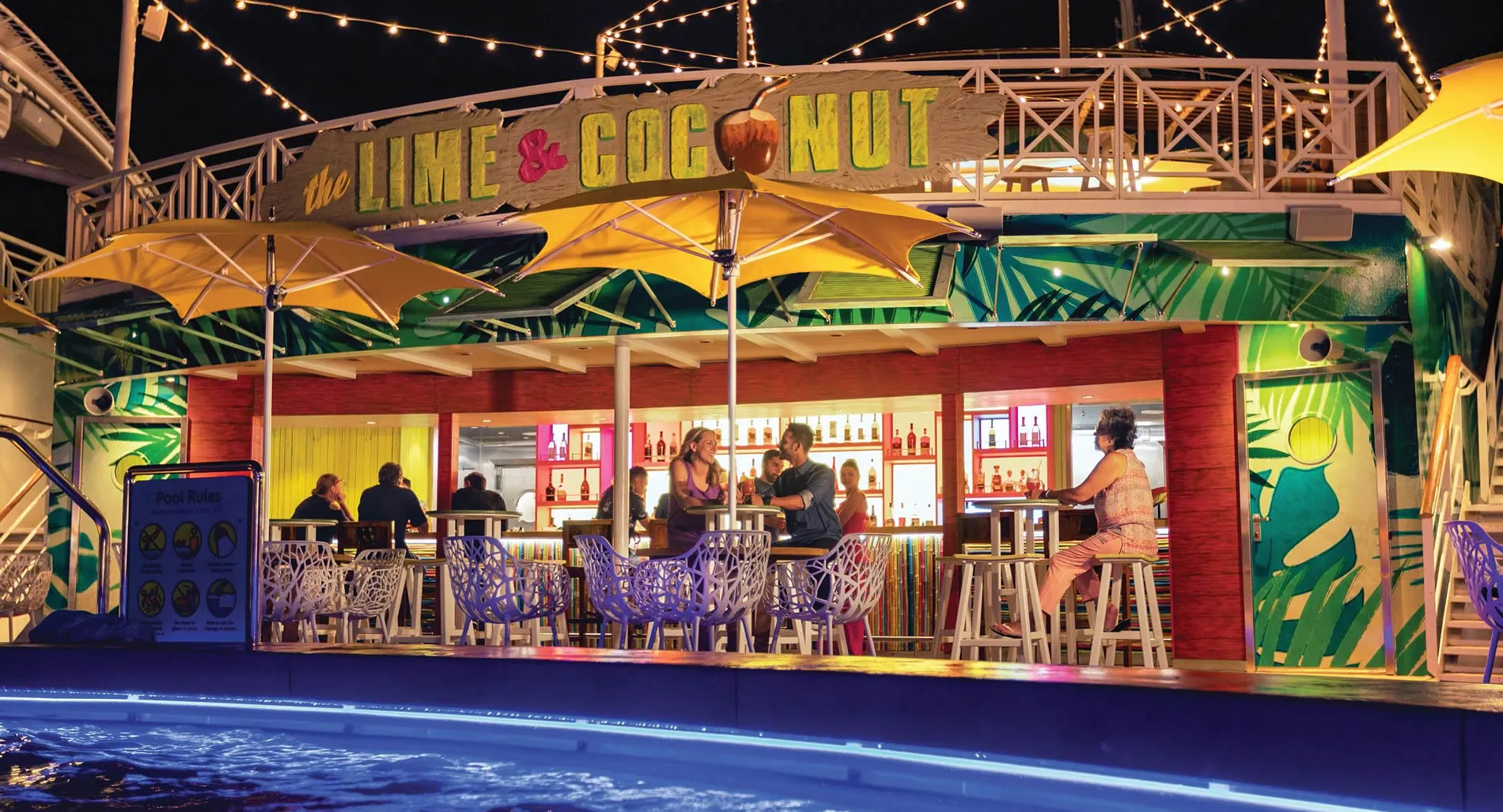 Colorful Lime & Coconut bar with yellow umbrellas and blue pool at night