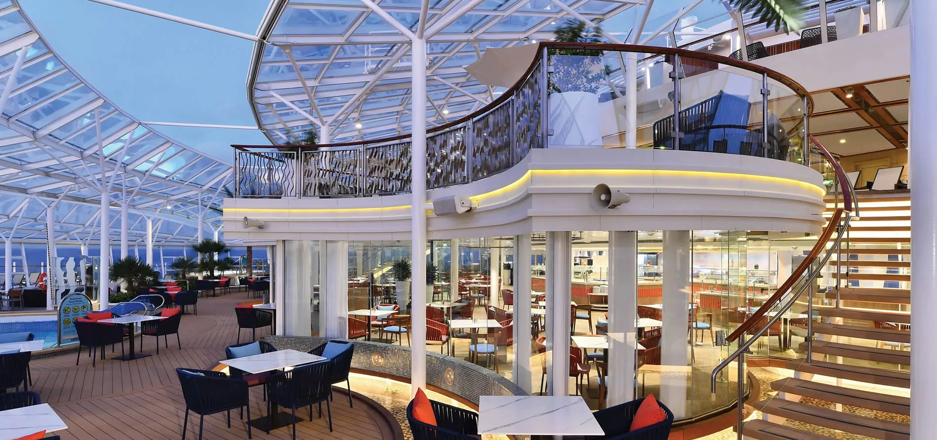Modern cruise ship deck with glass ceiling, dining area, and curved staircase