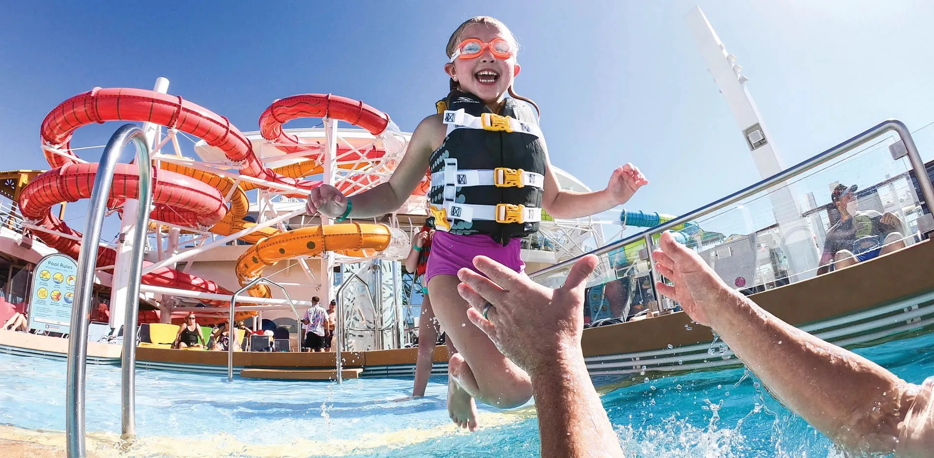 Excited child jumping in pool with colorful water slides in background