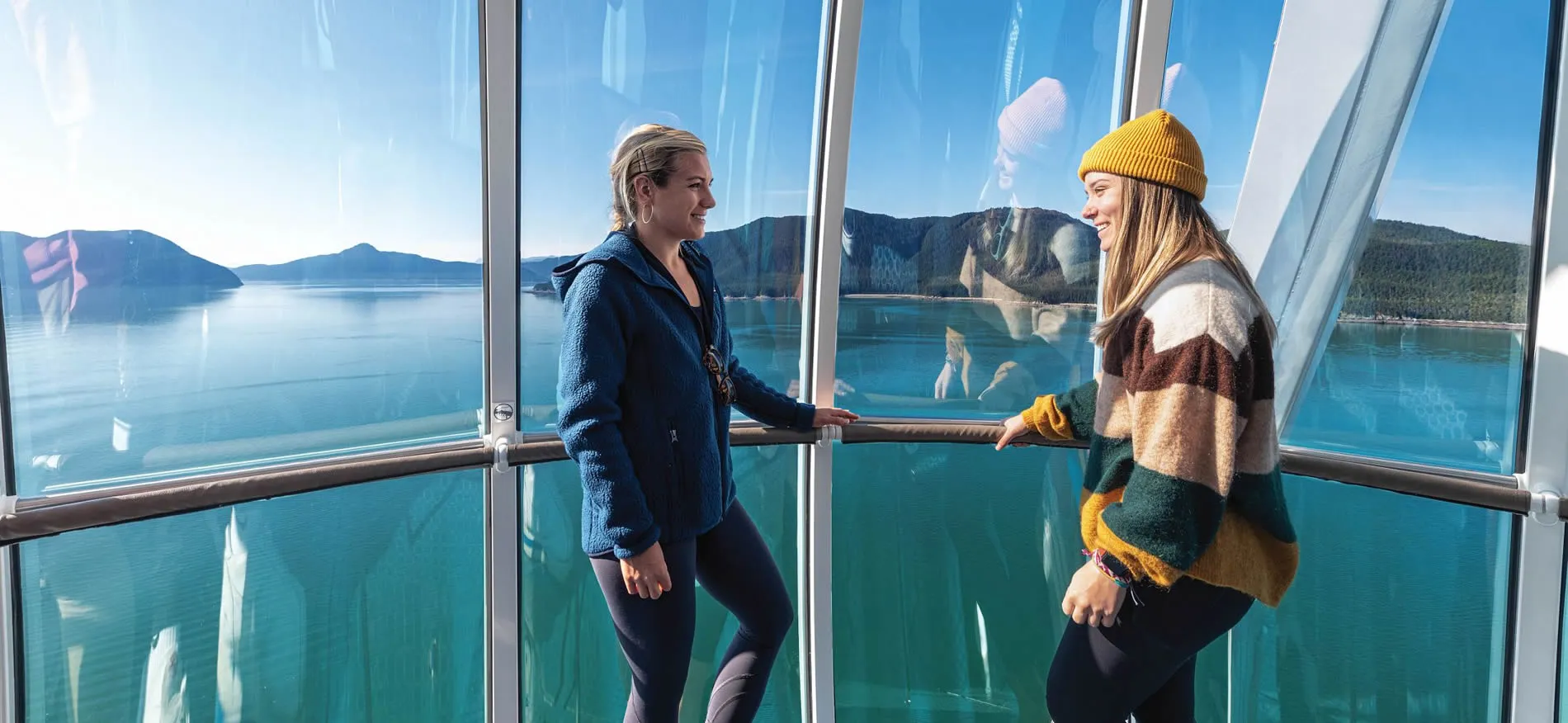 Two women enjoying scenic mountain lake view from glass observation deck