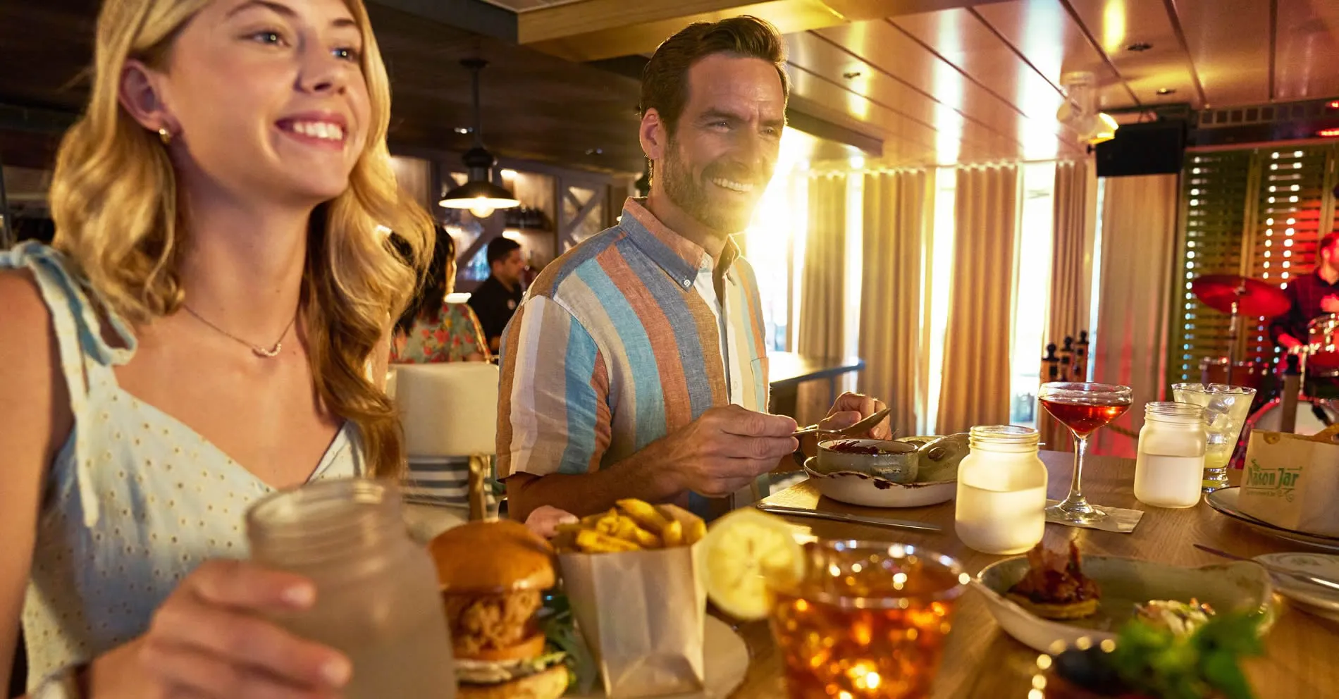 Two people enjoying a meal with drinks at a warm, sunlit restaurant