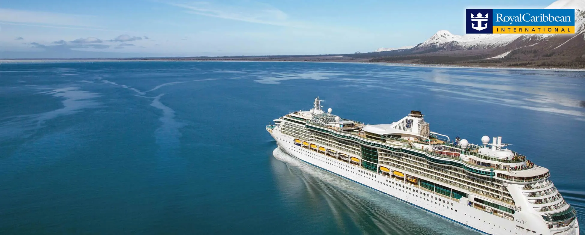 Royal Caribbean cruise ship sailing in calm blue waters near snowy mountains