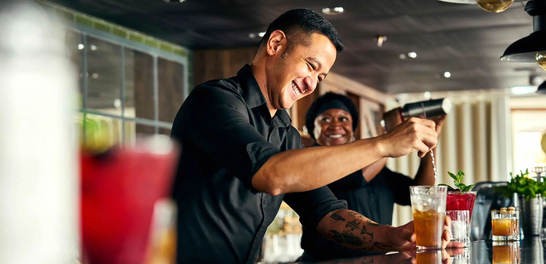 Bartender mixing cocktails with a smile, colleague in background
