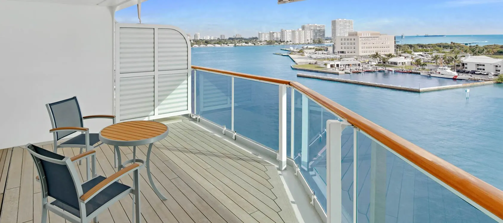 Cruise ship balcony with chairs overlooking marina and coastal cityscape