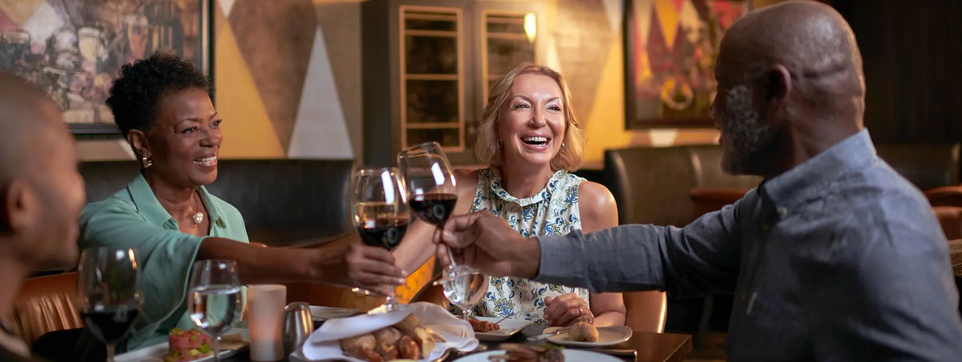 Friends toasting wine and laughing together at restaurant dinner table