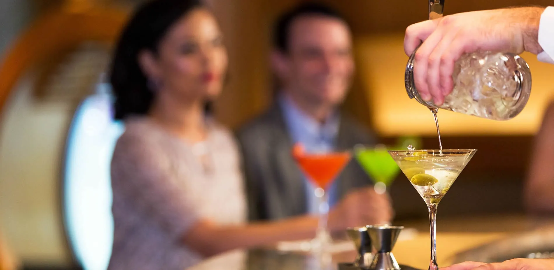 Bartender pouring cocktail with colorful martini glasses in background