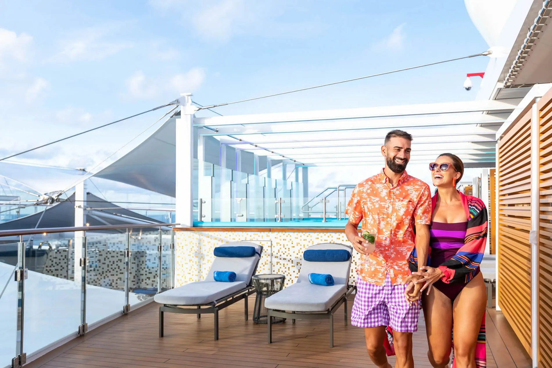 Couple enjoying drinks on cruise ship deck with lounge chairs