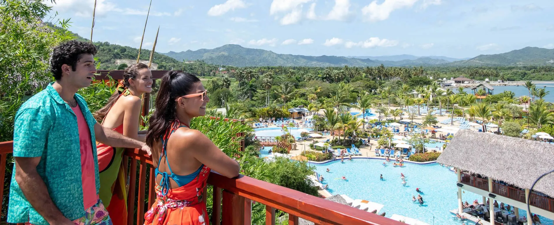Tourists overlooking tropical resort pool with mountains and palm trees