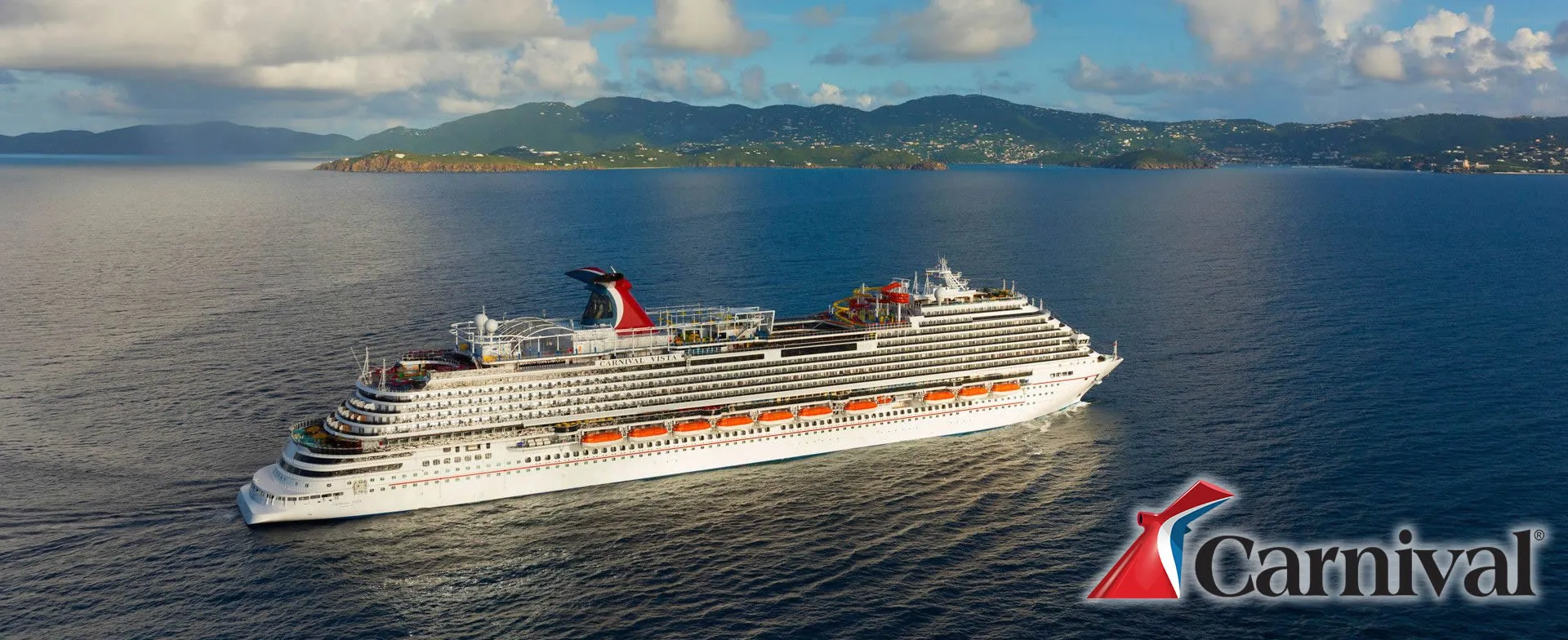 Large Carnival cruise ship sailing near tropical mountainous coastline