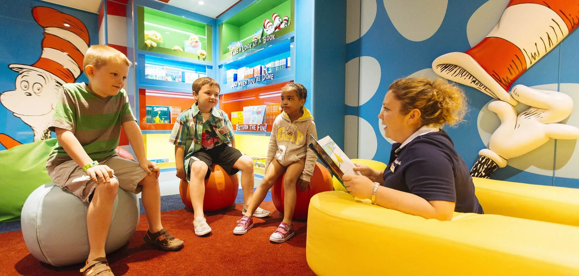 Children sit in colorful Dr. Seuss-themed library reading area with instructor