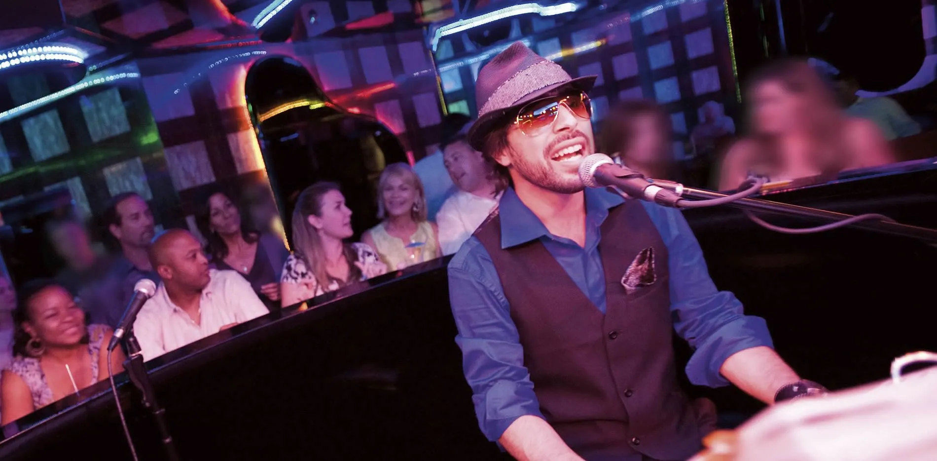 Musician in hat and sunglasses performing at a lively piano bar
