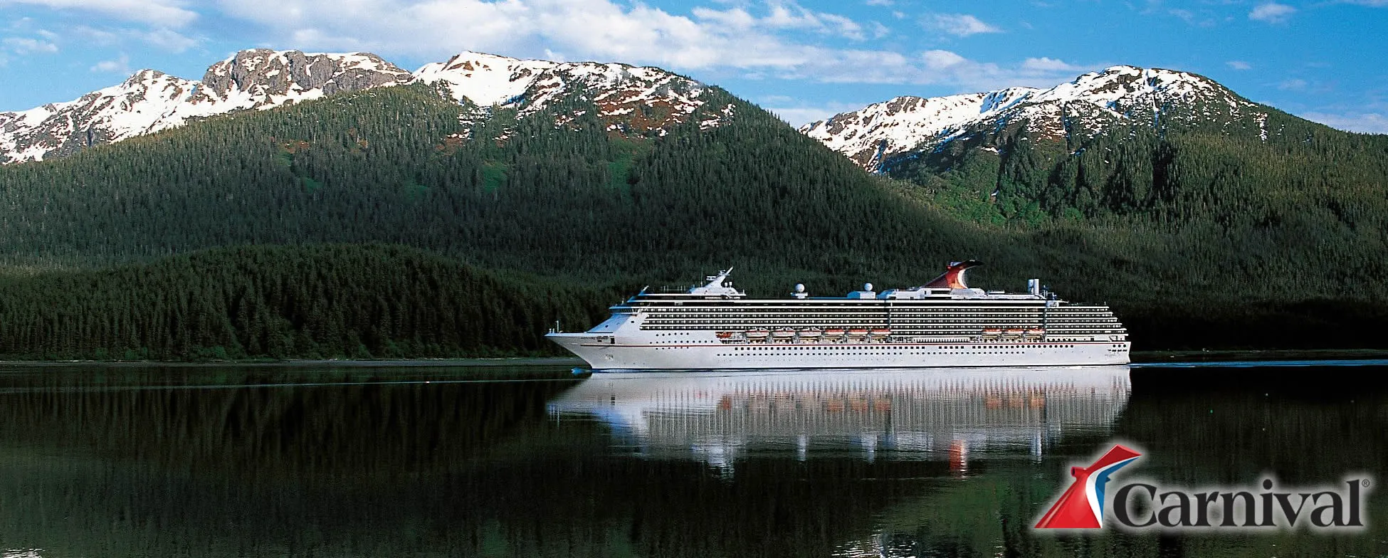 Carnival cruise ship sailing through calm Alaskan waters with snowy mountains