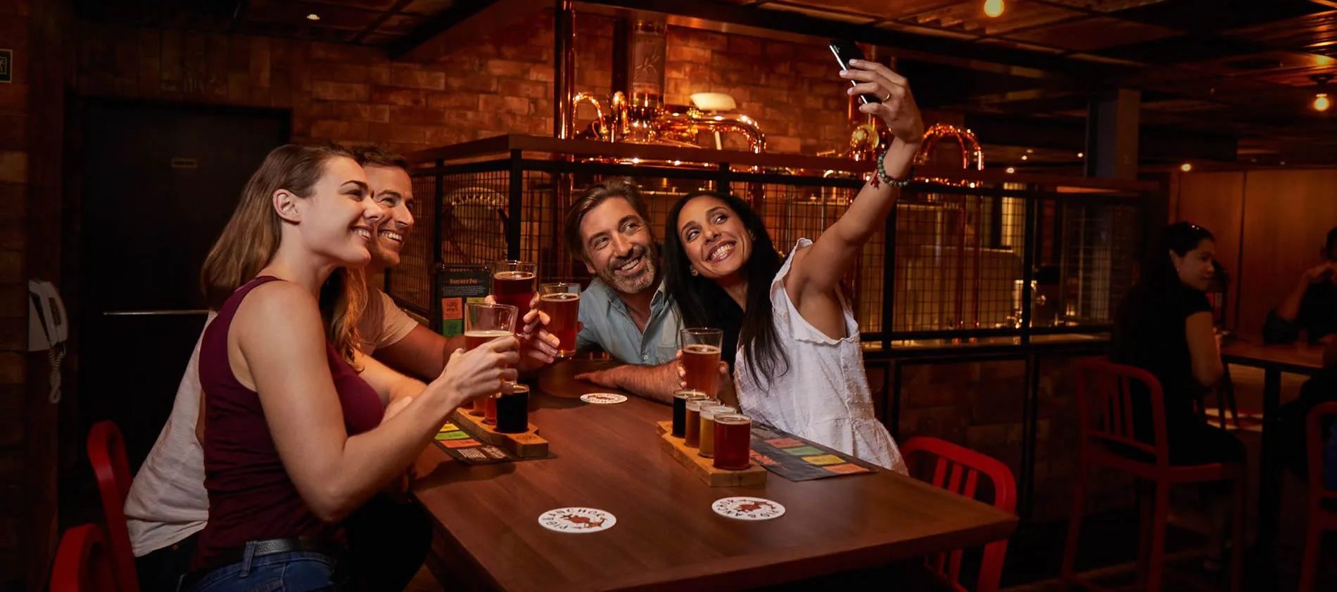 Friends enjoying beer and taking selfie at brewery with craft beer flight