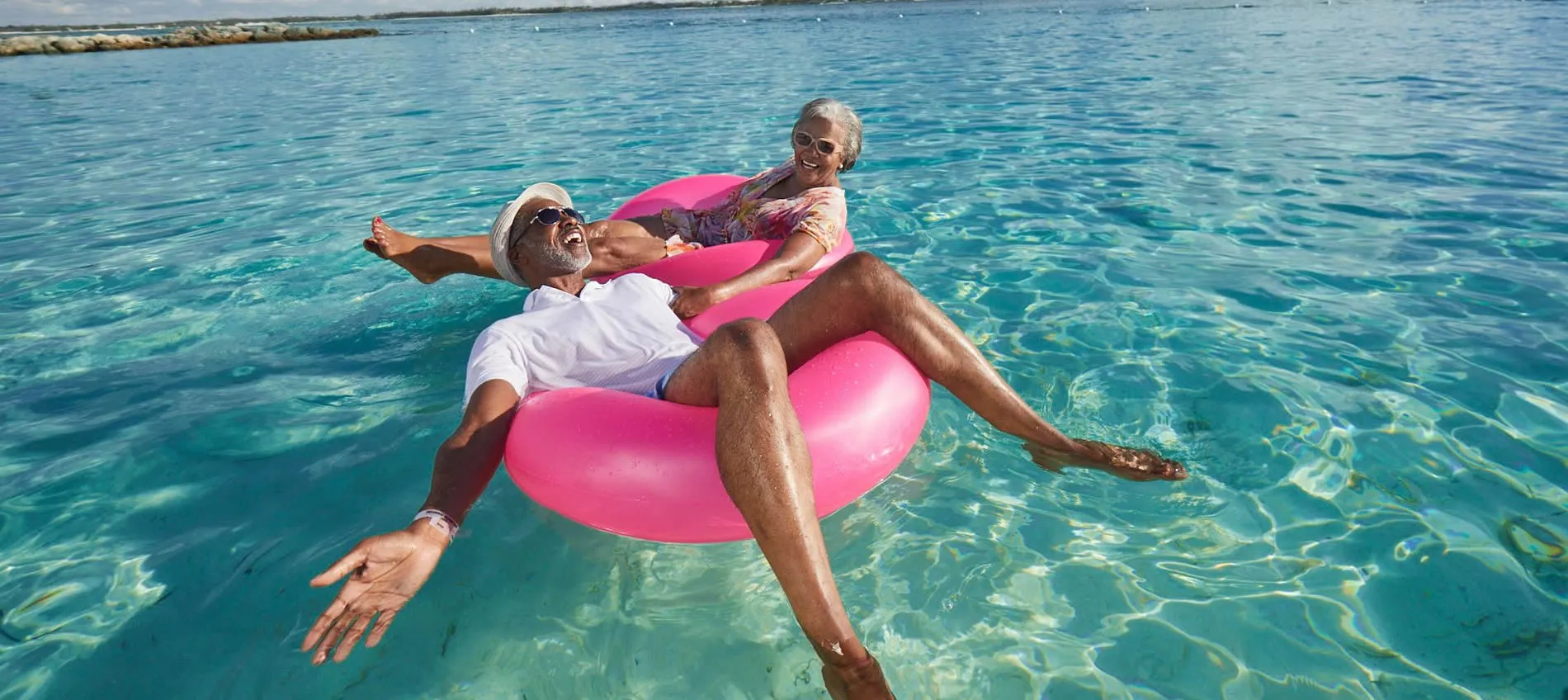 Seniors enjoying a playful moment on a pink float in clear blue water