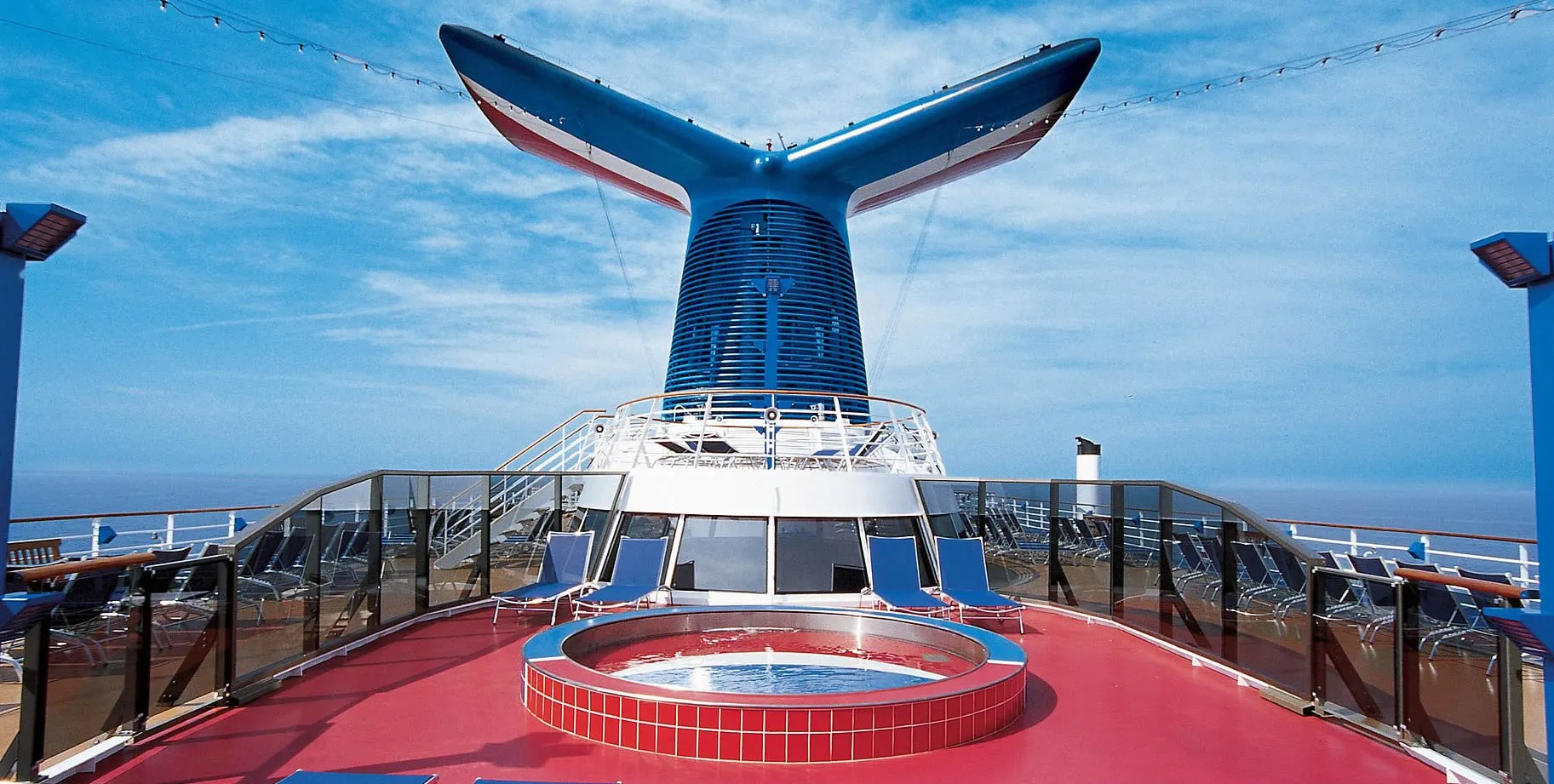 Cruise ship deck with blue and red funnel, pool, and ocean view