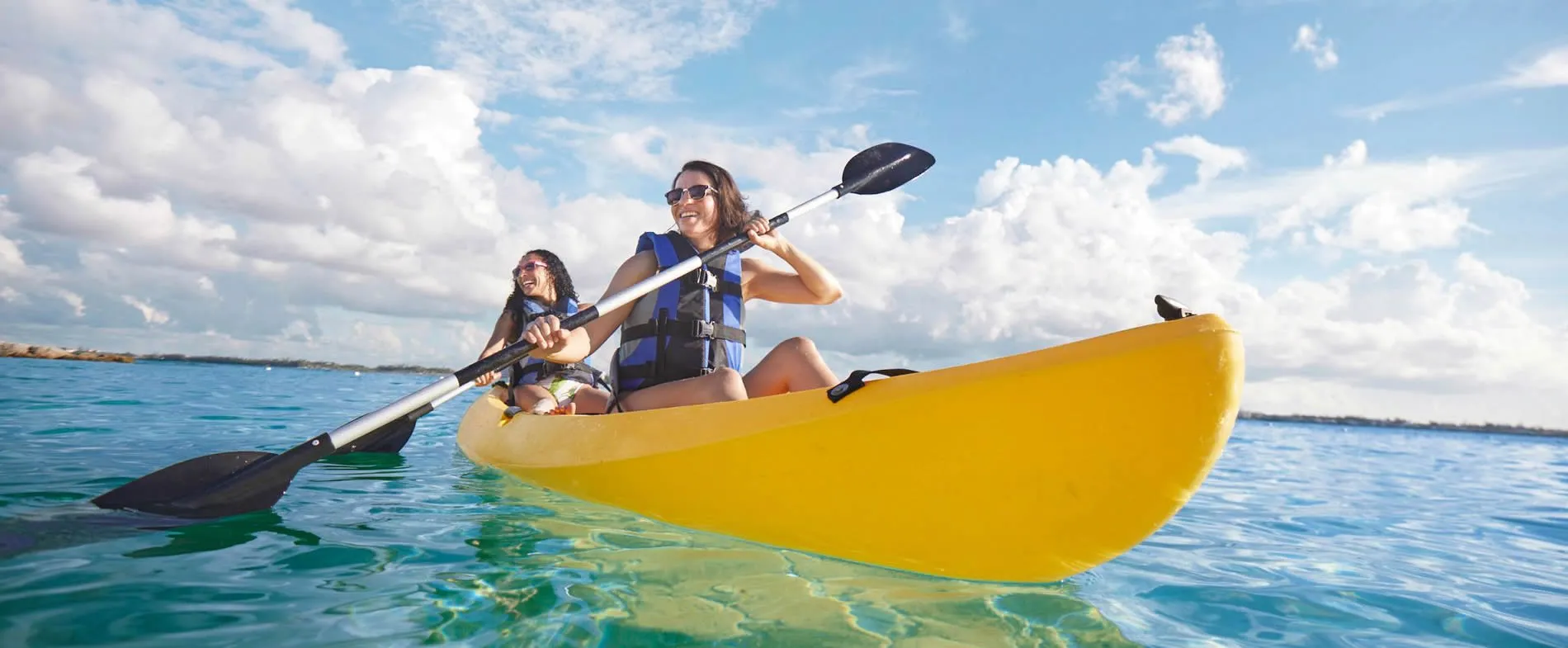 Two people kayaking on bright blue water under cloudy sky