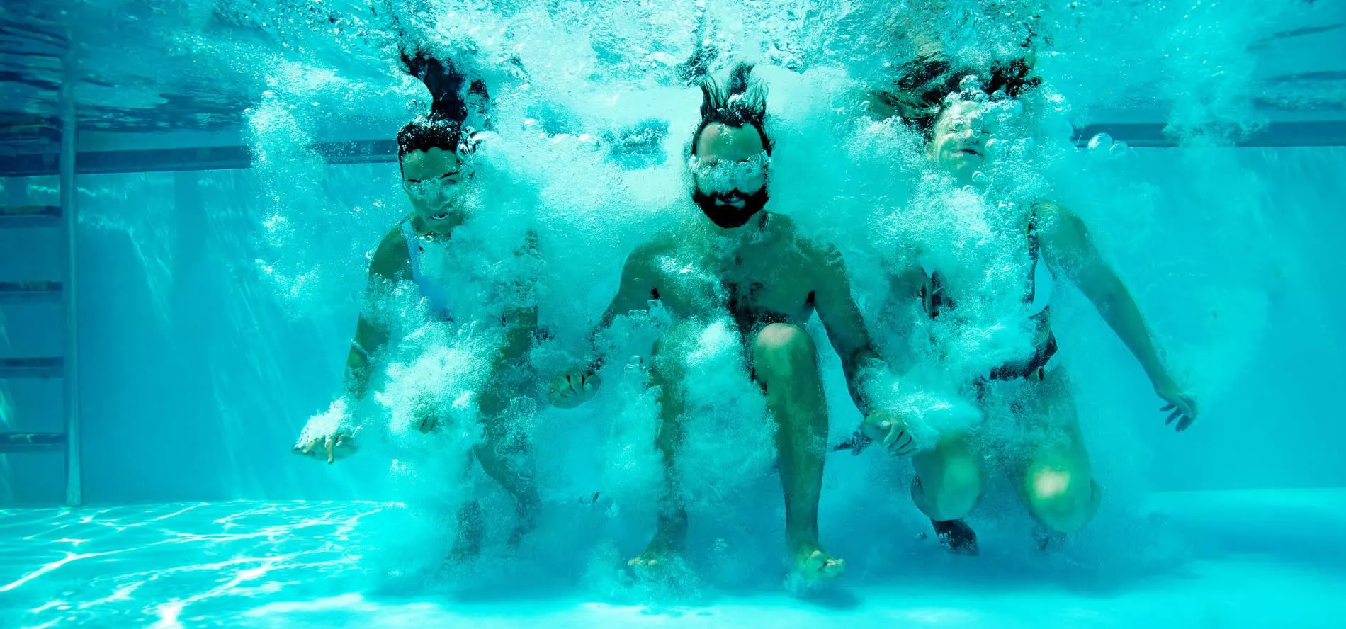 Three people diving underwater in a swimming pool with turquoise water