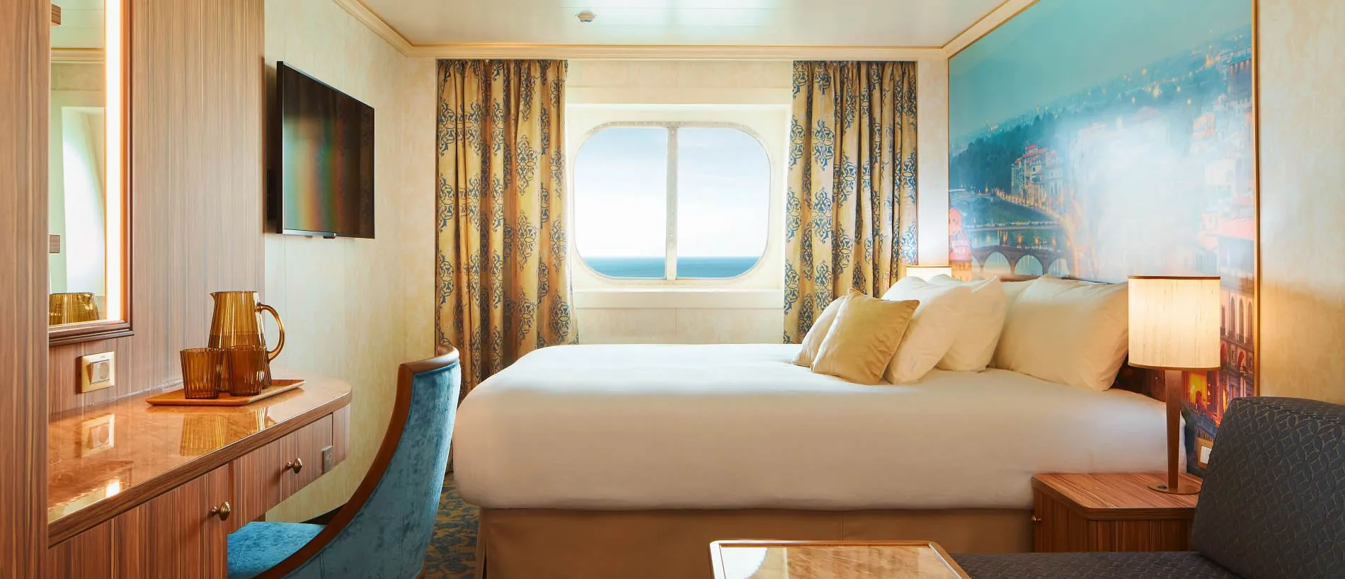 Luxurious cruise ship cabin with ocean view, white bed, and scenic artwork