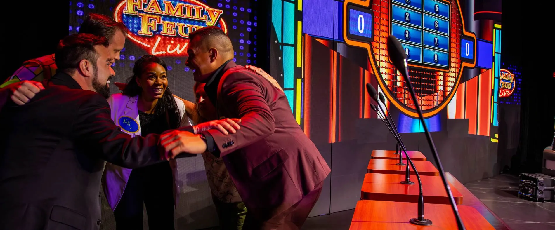 Contestants interacting on colorful Family Feud Live game show stage