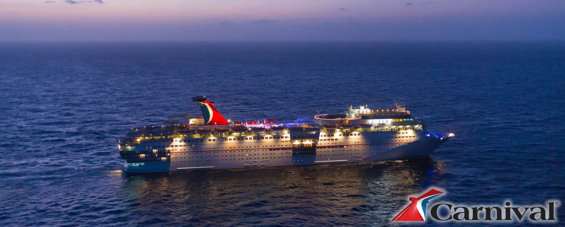 Carnival cruise ship illuminated at dusk on calm blue ocean waters