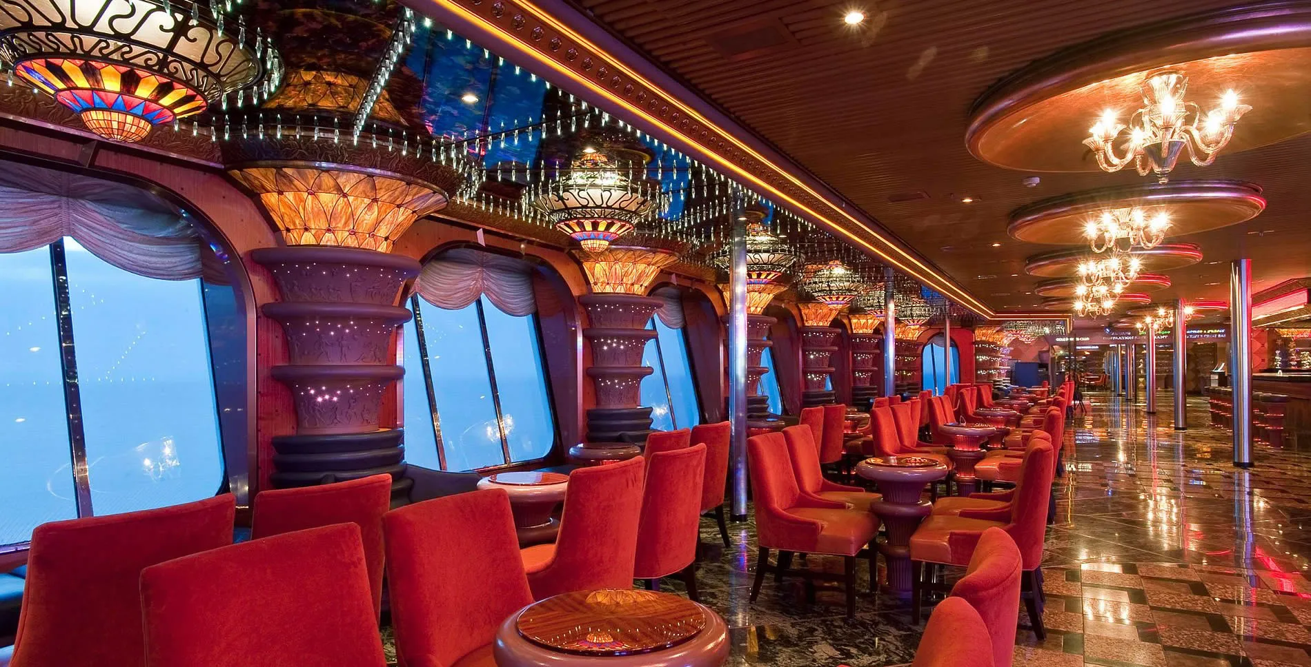 Luxurious cruise ship lounge with red chairs, chandeliers, and ocean view