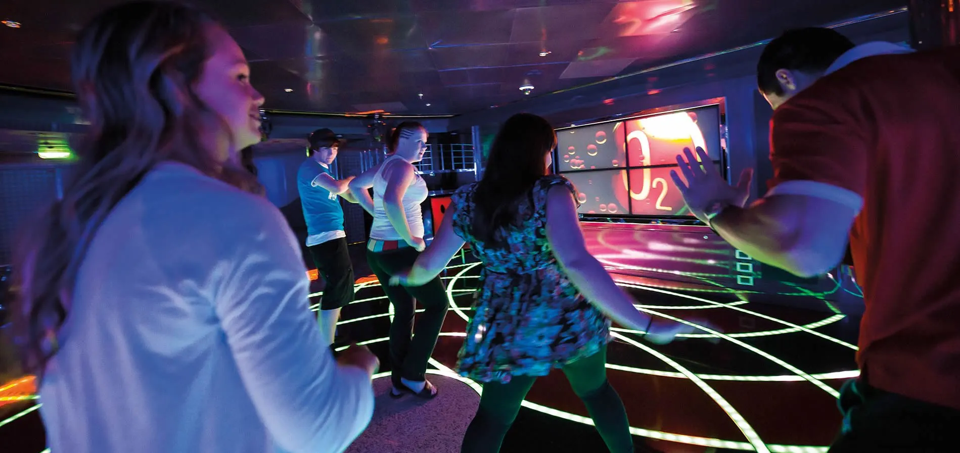 People dancing on illuminated floor with colorful lights and screen backdrop
