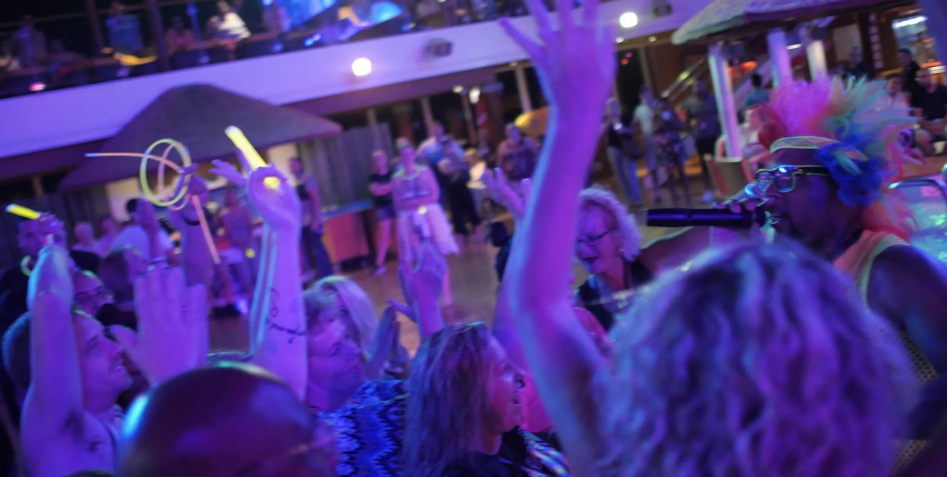 Crowded party with people dancing and raising hands in purple-blue light