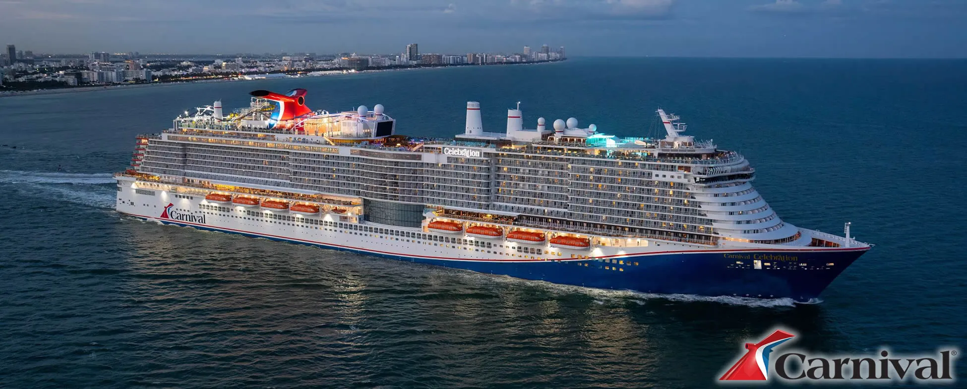 Large Carnival cruise ship sailing near coastal city at sunset