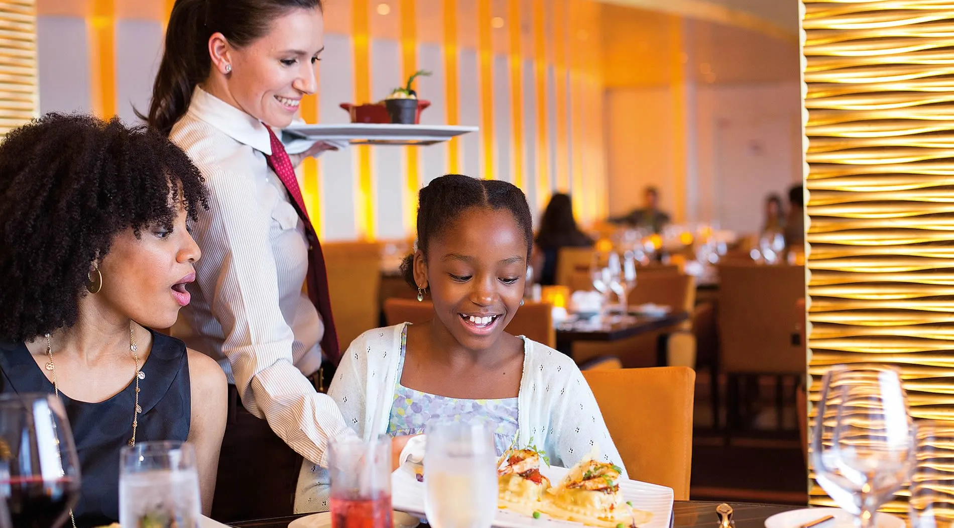 Smiling waitress serving food to happy guests in elegant restaurant