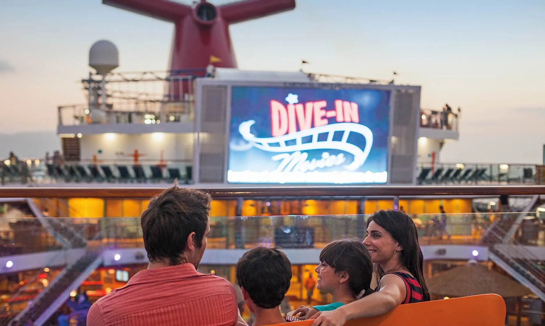 Family watching dive-in movie on cruise ship deck at sunset