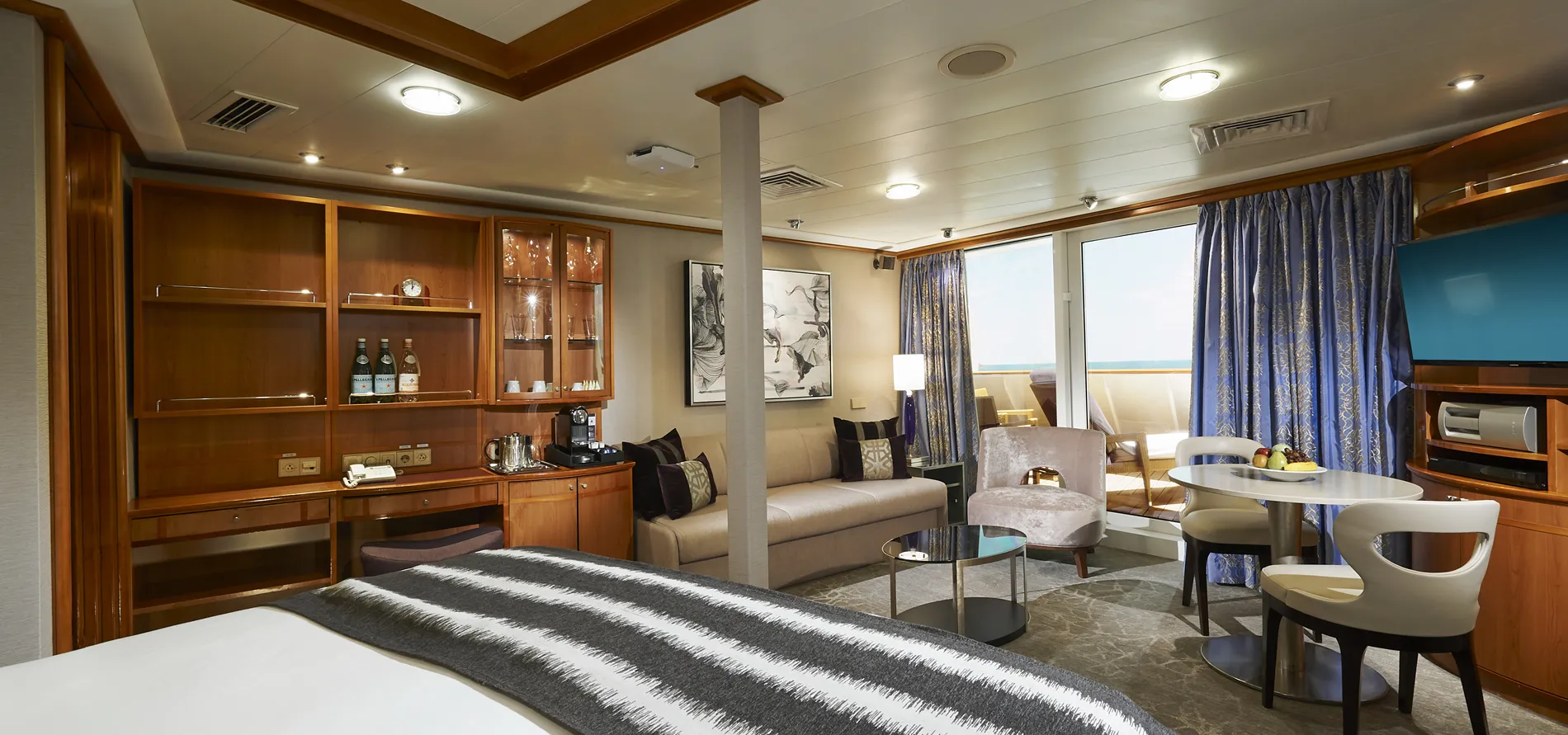 Luxury cruise ship cabin with ocean view, wooden cabinets, and seating area