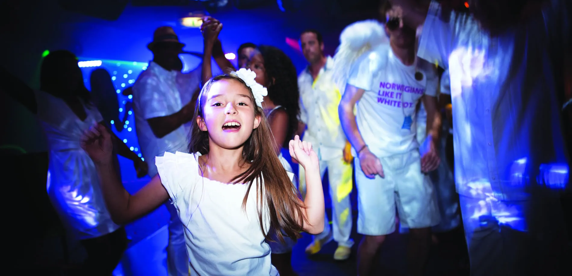 Young girl dancing joyfully at a white-themed party with blue lights