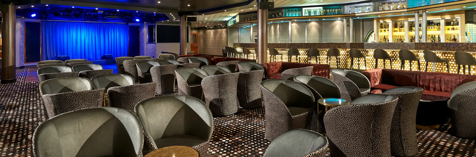 Cruise ship lounge with blue stage, leopard-print chairs, and illuminated bar