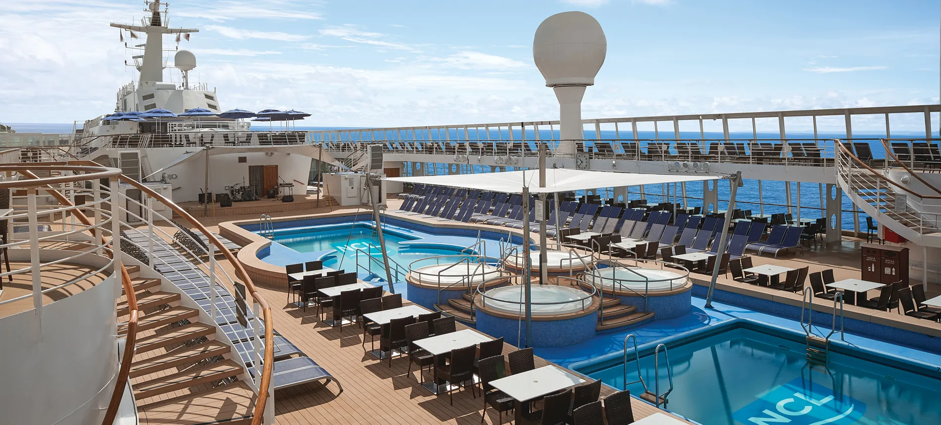 Luxury cruise ship deck with swimming pools, lounge chairs, and ocean view
